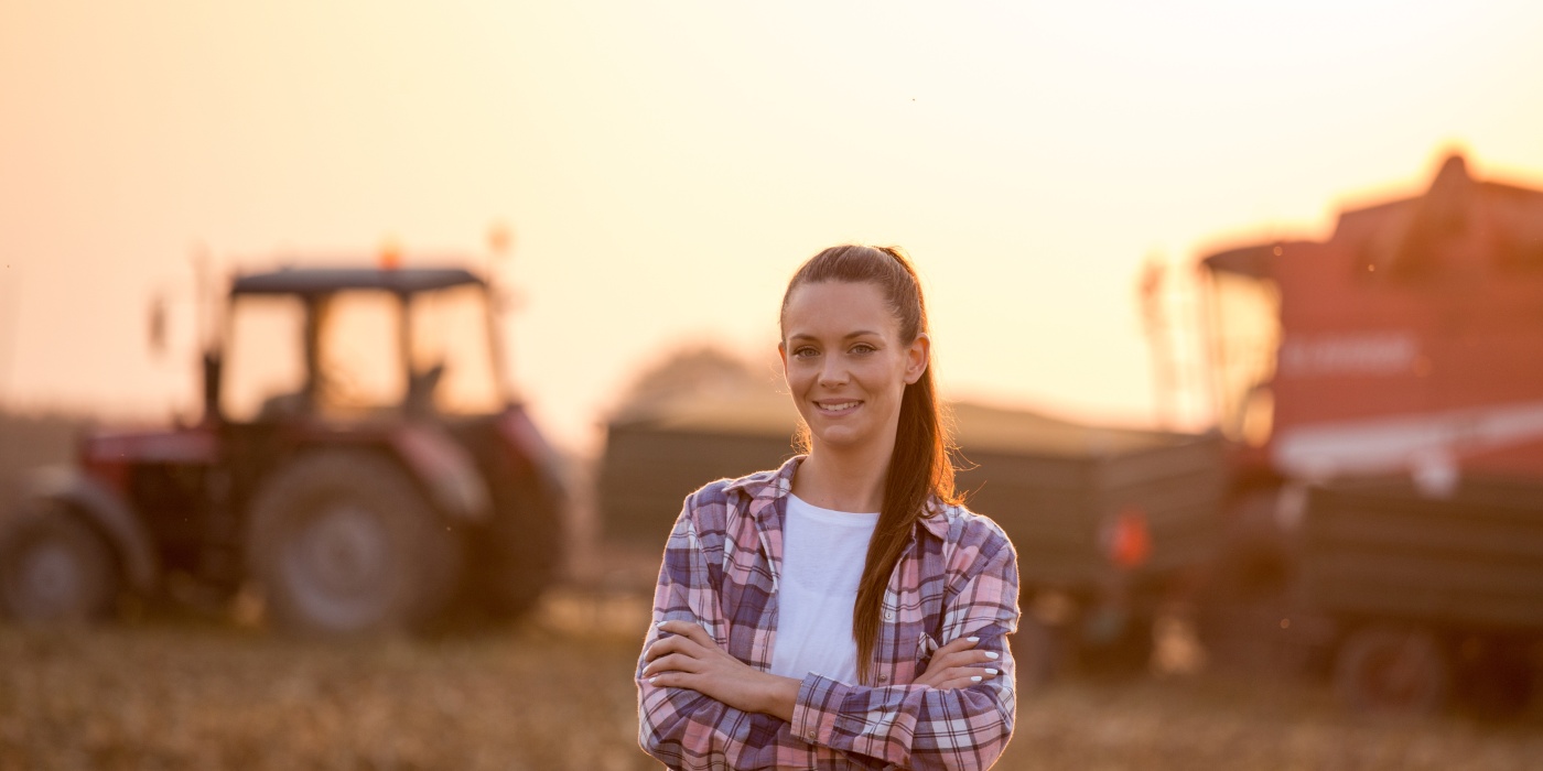 Woman in a chequered shirt looks into the camera and stands in front of a tractor